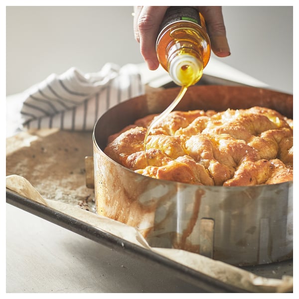 A person drizzles syrup on baked, round pastry in a silver baking pan.