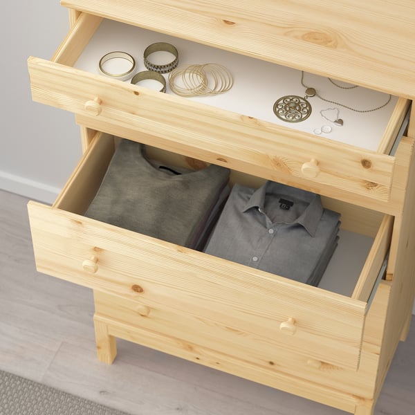 Wooden chest of drawers with two open drawers. Top drawer contains jewellery, bottom drawer holds folded clothes.