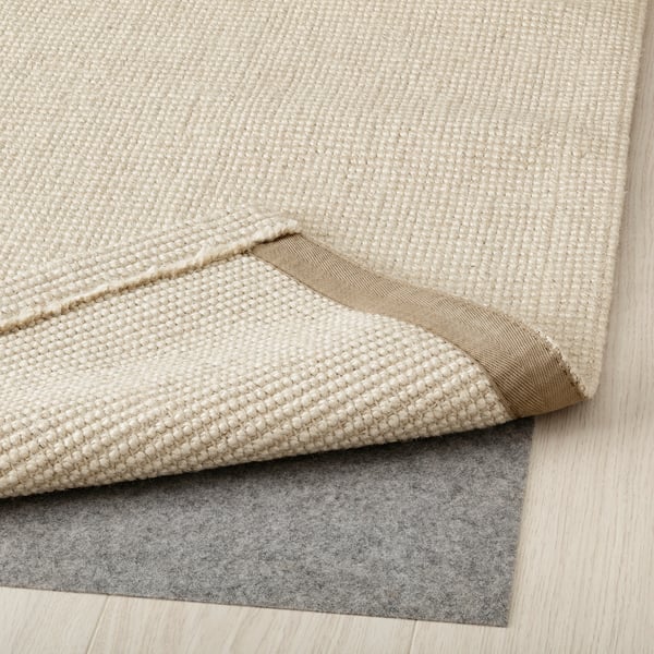 Natural jute rug layered over grey anti-slip mat on wooden floor. Easy to clean and vacuum.