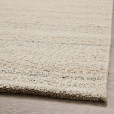 Flatwoven beige rug with subtle texture, laid on wooden floor. Quality materials give soft, warm feel.