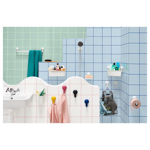 Bright bathroom with colourful hooks and holders; includes pink, yellow, blue, and black TISKEN accessories on white tiles.