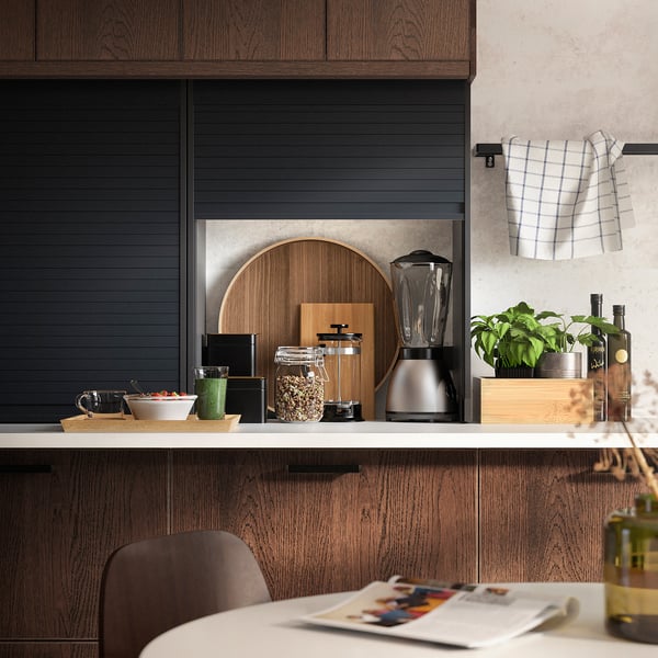 Modern kitchen with dark wood cabinets, white countertop, blender, plants, bottles, chair, towel, and magazine.