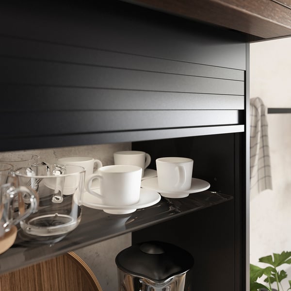 A sleek, black kitchen cabinet with a tambour door, featuring white cups on a shelf. Modern design, hiding small appliances.