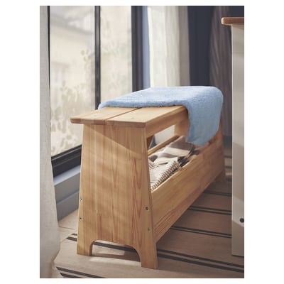Light-colored wooden bench with a soft blue blanket draped over it, positioned near a window with striped flooring.