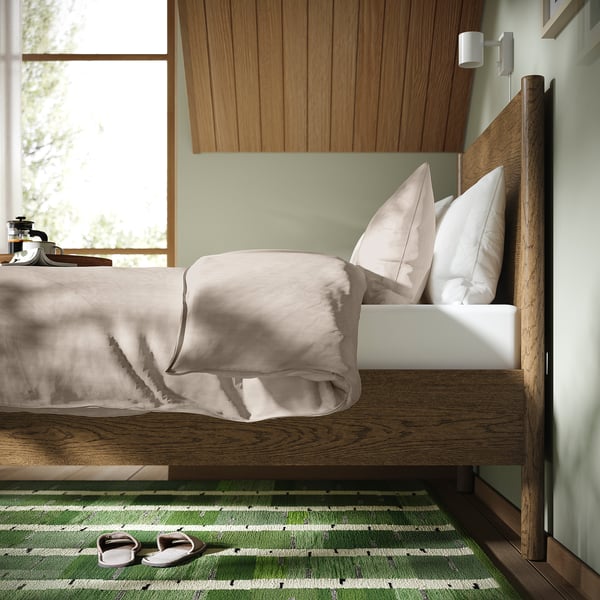 Bed with wooden frame, light bedding, slatted base, soft rug, and slippers.