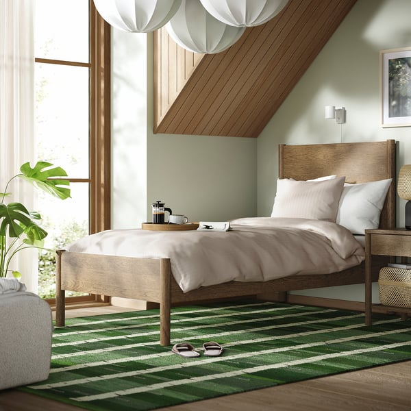 Cosy bedroom with TONSTAD bed, light brown frame, green rug, white pillows, stylish pendant light.