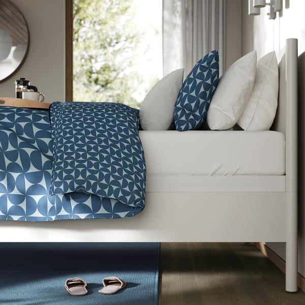 Cosy bed with blue geometric cover, white pillows, coffee maker tray, clean design.