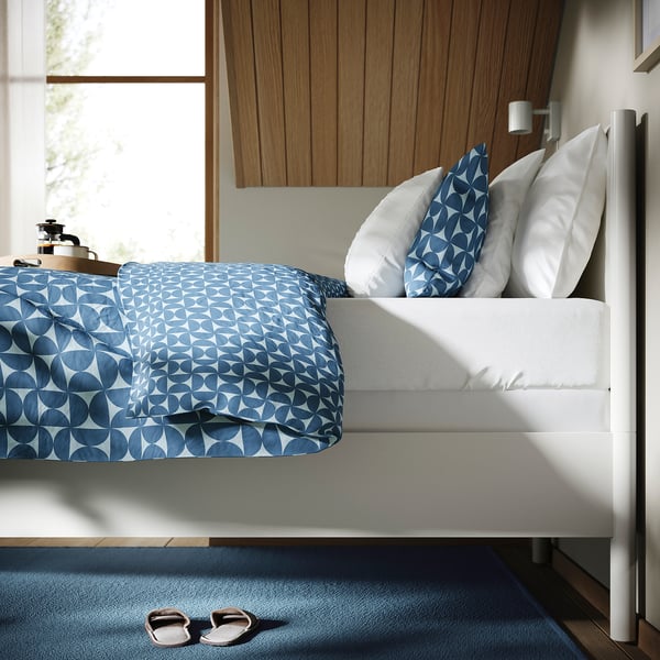 Adjustable white bed frame with blue quilt, pillows, slippers on rug