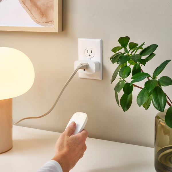 A hand plugs in a white TRETAKT remote control plug into a wall outlet, demonstrating its use to control household appliances.
