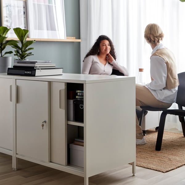 People discuss in office, divided by TROTTEN storage cabinet.