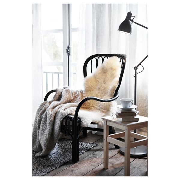 Cosy indoor scene: chair with sheepskin, books, mug, lamp, soft light.