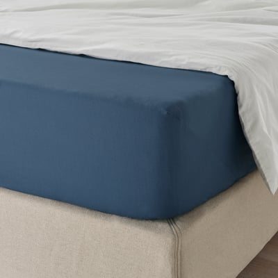 Bed with dark blue fitted sheet on white mattress, showing elastic edge.