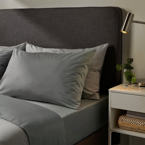 Modern bedroom scene with ULLVIDE grey bedding, plush pillows, trendy headboard, sleek side table, plant, and lamp.