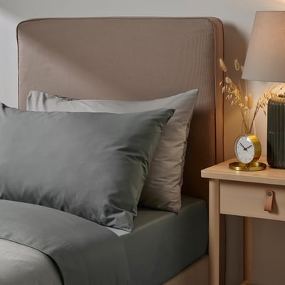Bed with grey ULLVIDE sheets, texture pattern headboard, small bedside table, gold clock, beige lamp, dried flowers vase.