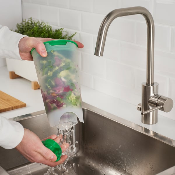 Person rinses salad in UPPFYLLD shaker under sink tap. Green container with water flowing, demonstrating efficient vegetable rinsing.