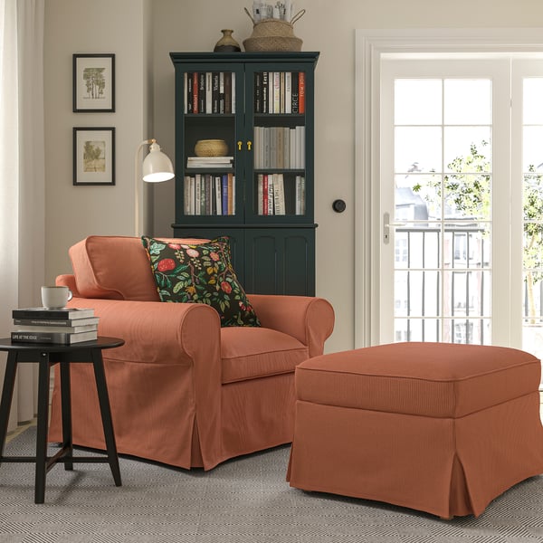 Comfy reading nook with coral armchair, ottoman, dark cushions, black table, & tall bookshelf.