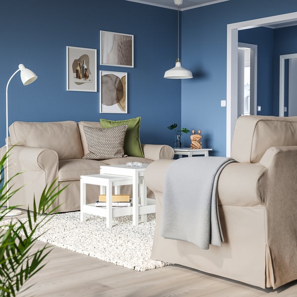Modern living room with UPPLAND beige sofa, white coffee table, grey rug, and blue walls. Decorated with art, plants, and a pendant light.