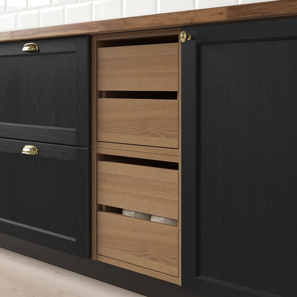 Black kitchen cabinet with three wooden drawers, one partly open showing cutlery, sitting on light wooden floors.