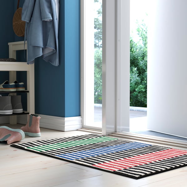 Multicoloured striped door mat by shoe rack on white floor.