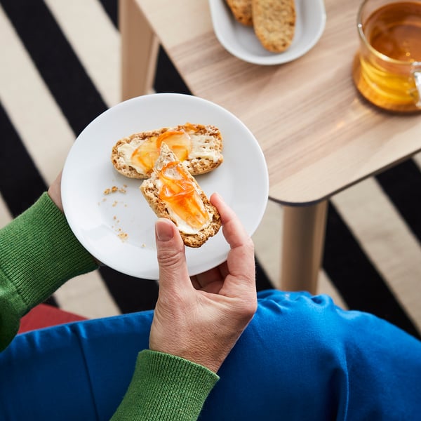 Image hands holding a plate with two orange-colored cracker pieces, likely containing orange and elderflower spread.