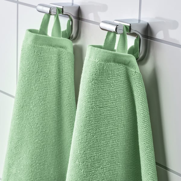 Two green towels hang neatly, displaying absorbent, fast-drying ribbed weave.