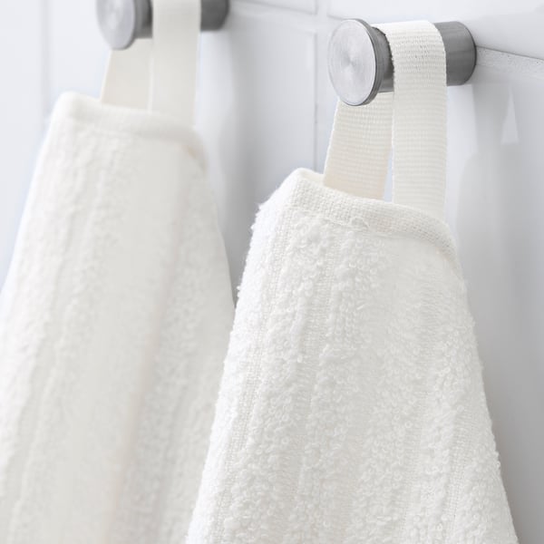 White towels hang on silver hooks against a white wall, showcasing their soft terry texture and practical design.