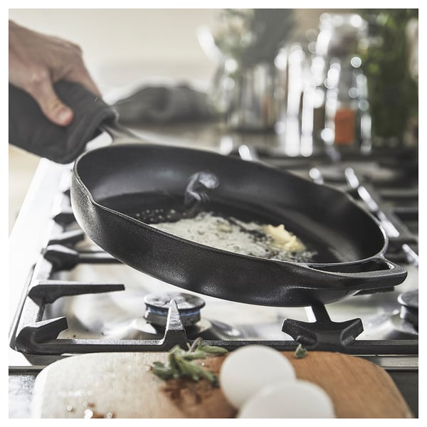 Black cast iron frying pan cooks on stove, with melted butter.