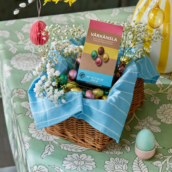 Blue cloth basket with chocolate eggs & hazelnut filling, surrounded by babys breath on green floral tablecloth.