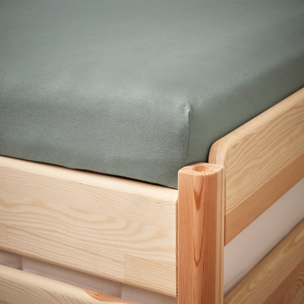 Close-up of a green fitted bed sheet corner on a wooden bed frame.