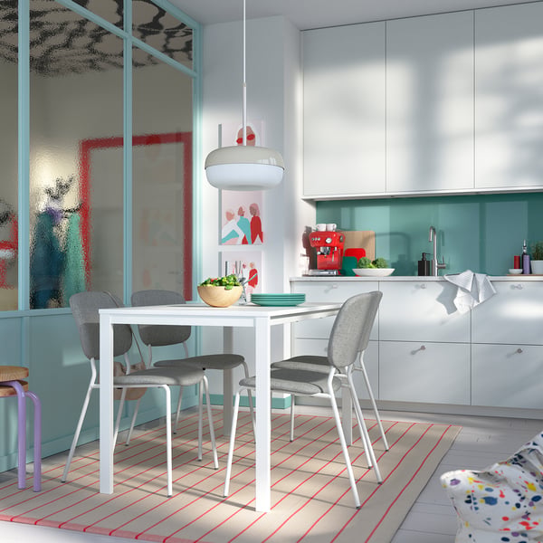 Modern kitchen with white table, grey chairs, red rug, turquoise cabinets.