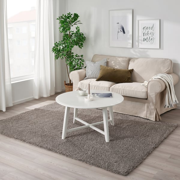 Grey VINDEBÄK rug under beige sofa, adding comfort & warmth. Anti-slip backing. White coffee table on top.