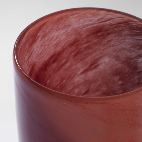 Close-up of a handcrafted, reddish glass candle holder, showcasing its smooth, mouth-blown texture and unique painted pattern inside.