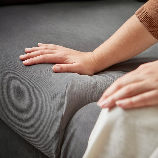 Persons hand resting on grey fabric sofa.
