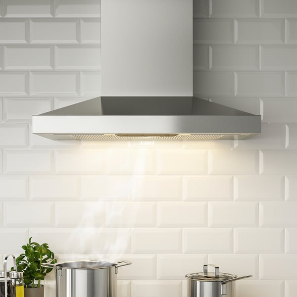 Modern stainless steel range hood with led light, mounted against white subway tiles.