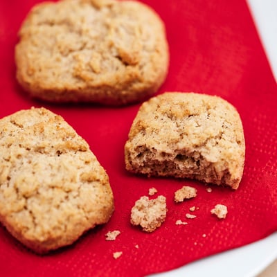 Three oat cookies on a bright red surface, one broken in half.