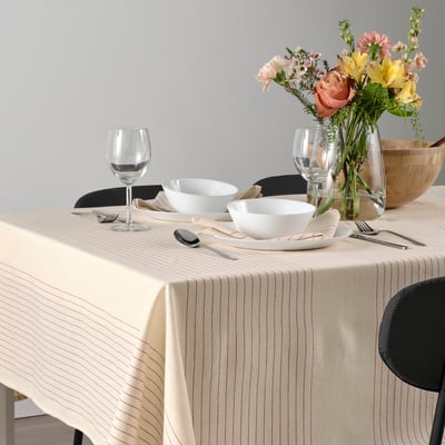 Elegant table setting with striped tablecloth, white bowls, silverware, wine glasses, and floral centrepiece.