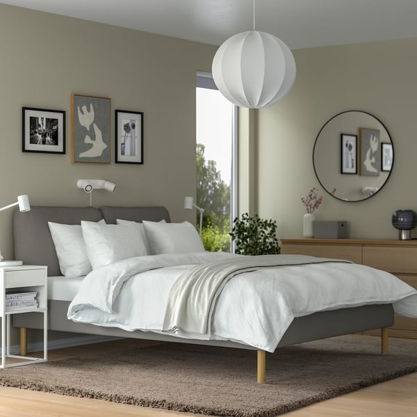 Modern bedroom with beige shaggy rug under grey bed. Pendant light, mirror, and bedside table with lamp. Calm, minimalist design.