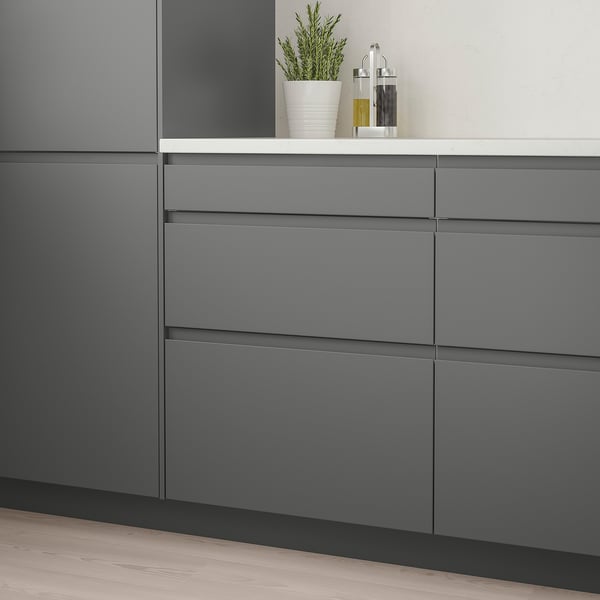 Modern kitchen with grey VOXTORP drawers, clean lines, integrated handles, small plant & oil bottles on counter.