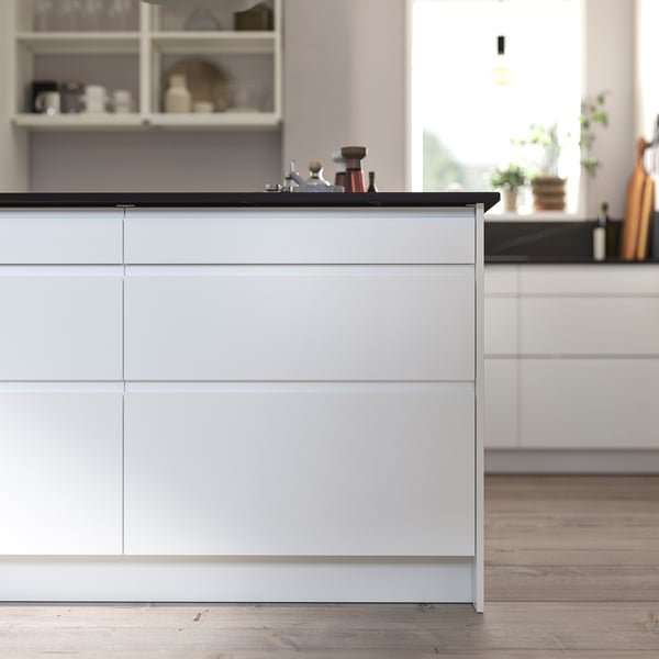Modern kitchen with white drawers and sleek handles, featuring a black countertop. Clean, minimalist design.