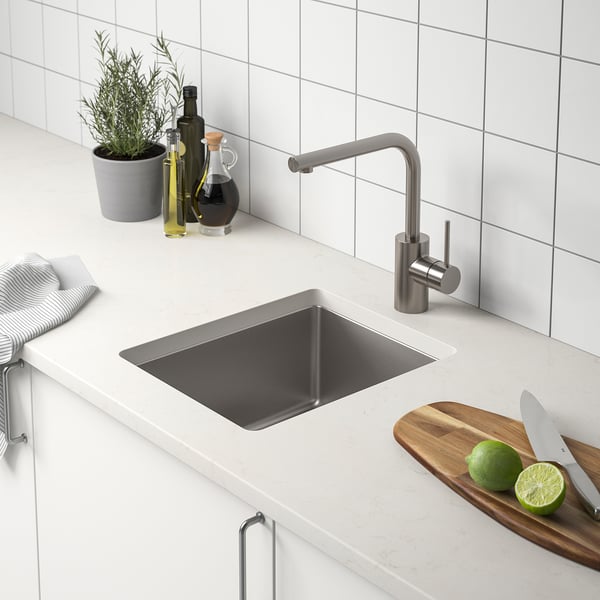 Modern kitchen sink in stainless steel with tap, limes, knife, bottles and plant.