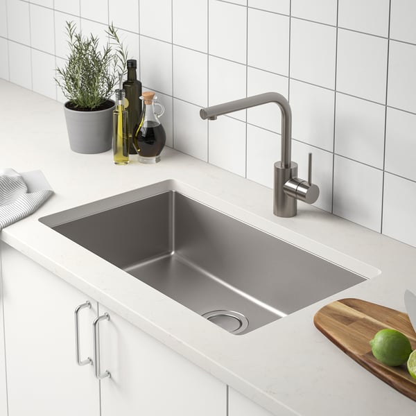 Stainless steel sink with silver tap, placed on white countertop beside limes and cutting board.