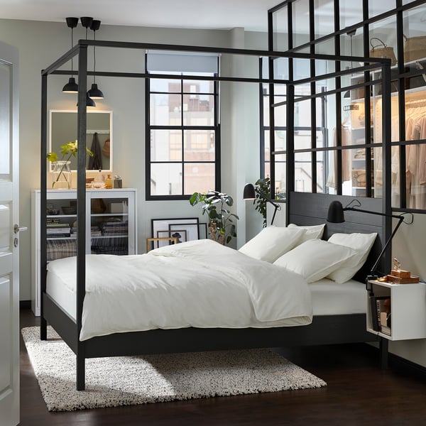 Modern bedroom with YTTERVÅG black four-poster bed, white linens, large windows, minimalist decor, and spacious layout.